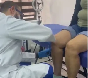 Especialista aplica plasma bioregenerativo en las piernas de un paciente como tratamiento regenerativo para lesiones o dolor crónico.